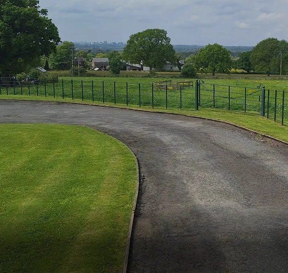 Curved driveway with green fields and trees.