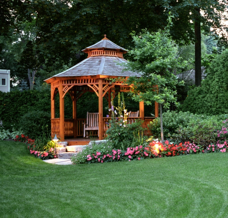 Wooden gazebo surrounded by flowers and trees.