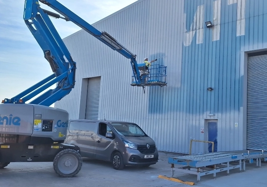 Worker on lift painting large industrial building.