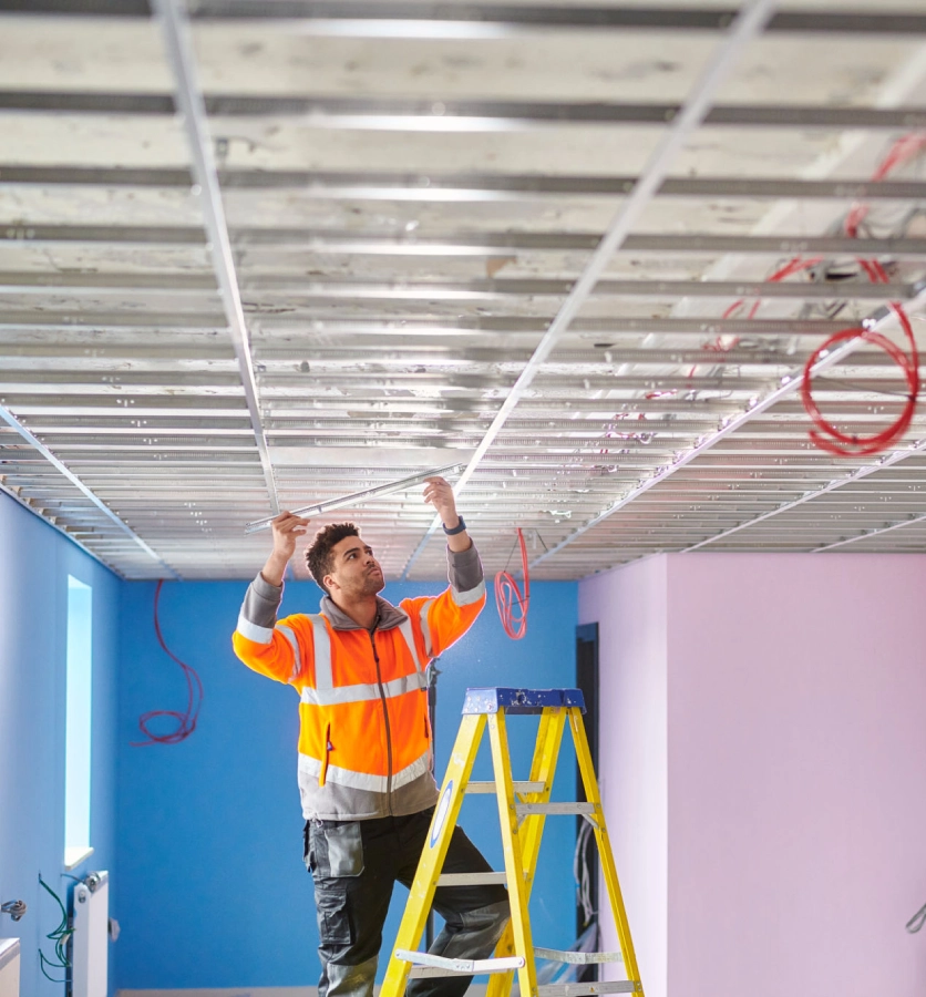 Worker installing ceiling wiring on ladder.