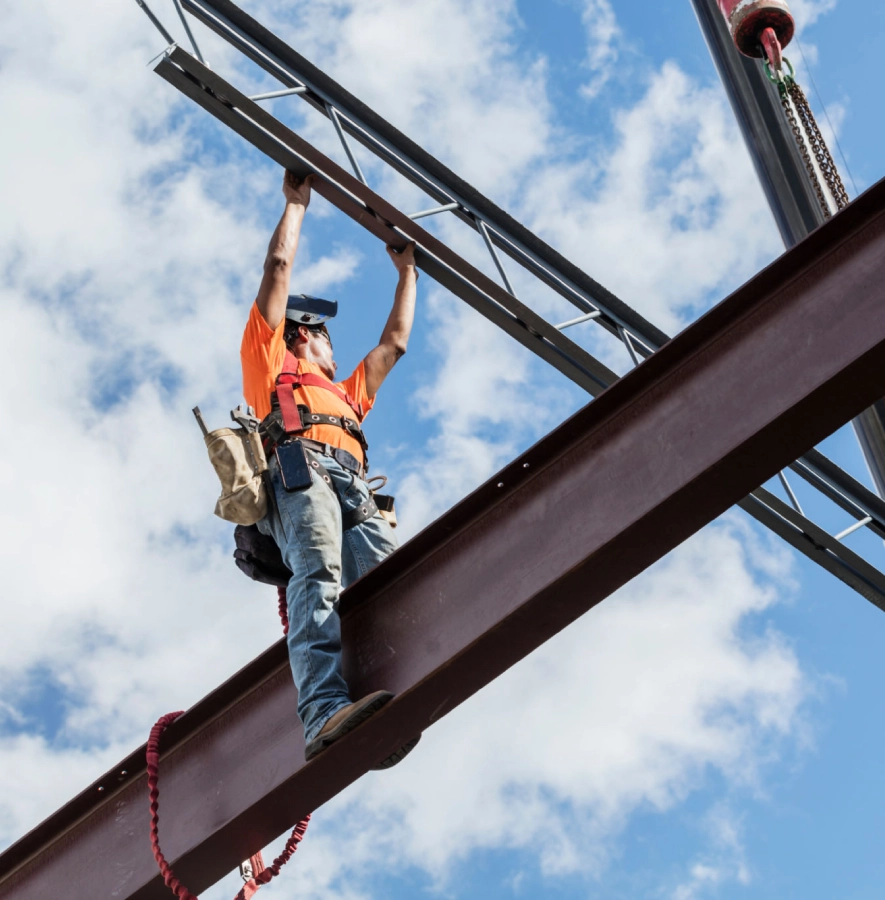 Construction worker on steel beam, blue sky.